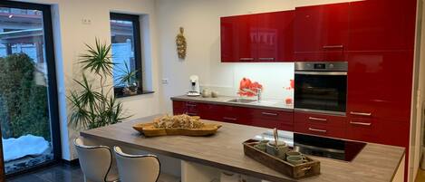 A modern kitchen with red cabinets, a central island with bar stools, and a view of the outdoors.