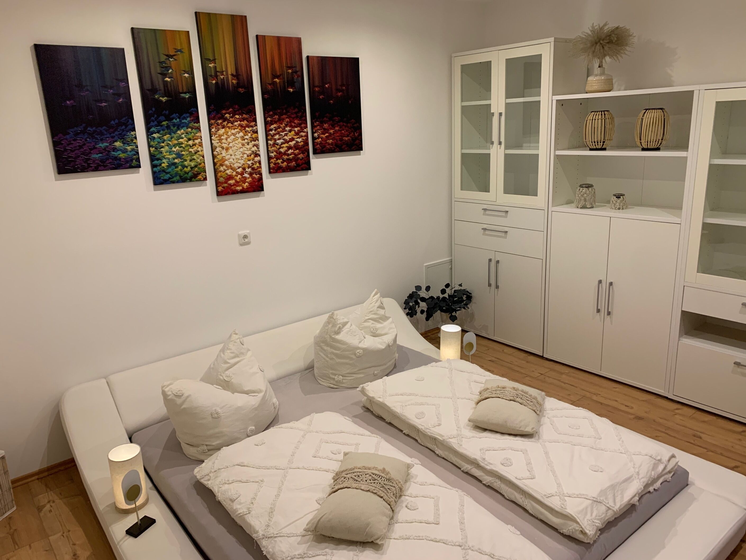 A bedroom with a bed, pillows, a bedside table, a lamp, a cabinet, and wall art.