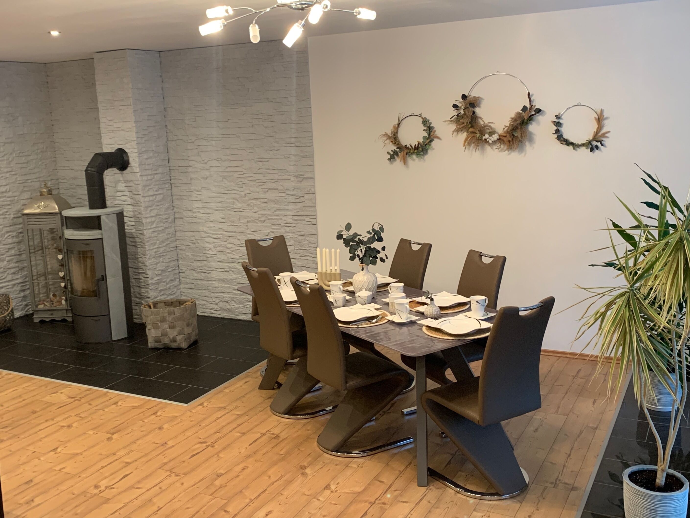 Un comedor con pared de piedra, chimenea y tres coronas decorativas colgadas en la pared.