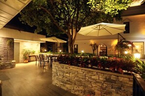 An outdoor patio area with a stone wall, a dining table, chairs, and a large umbrella providing shade.