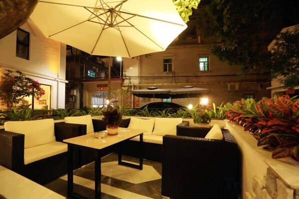 An outdoor seating area with tables and chairs, an umbrella, and potted plants.