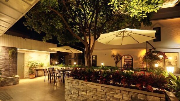 An outdoor patio area with stone walls, a table, chairs, and umbrellas. - Dongmenyuan Inn (Shenzhen)