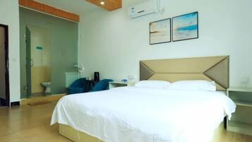 A hotel room with a bed, a desk, a chair, an air conditioning unit, and a glass door leading to a bathroom.