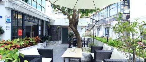 An outdoor seating area with tables and chairs, a large umbrella, and potted plants.