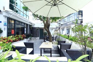 An outdoor seating area with tables and chairs, a large umbrella, and potted plants. - Dongmenyuan Inn (Shenzhen)