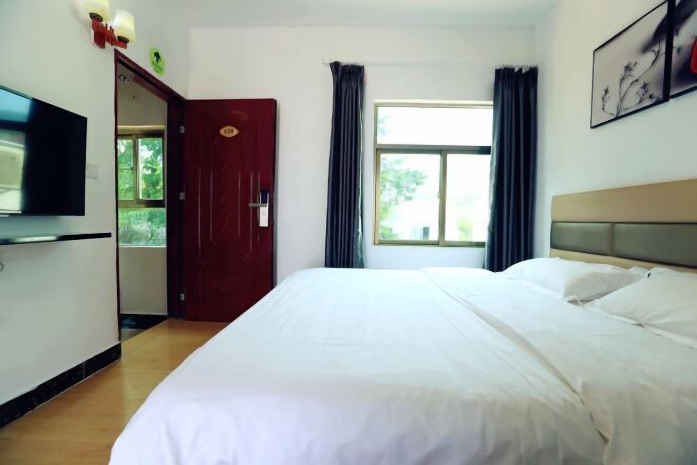 A hotel room with a bed, a television, a door, and a window with curtains.