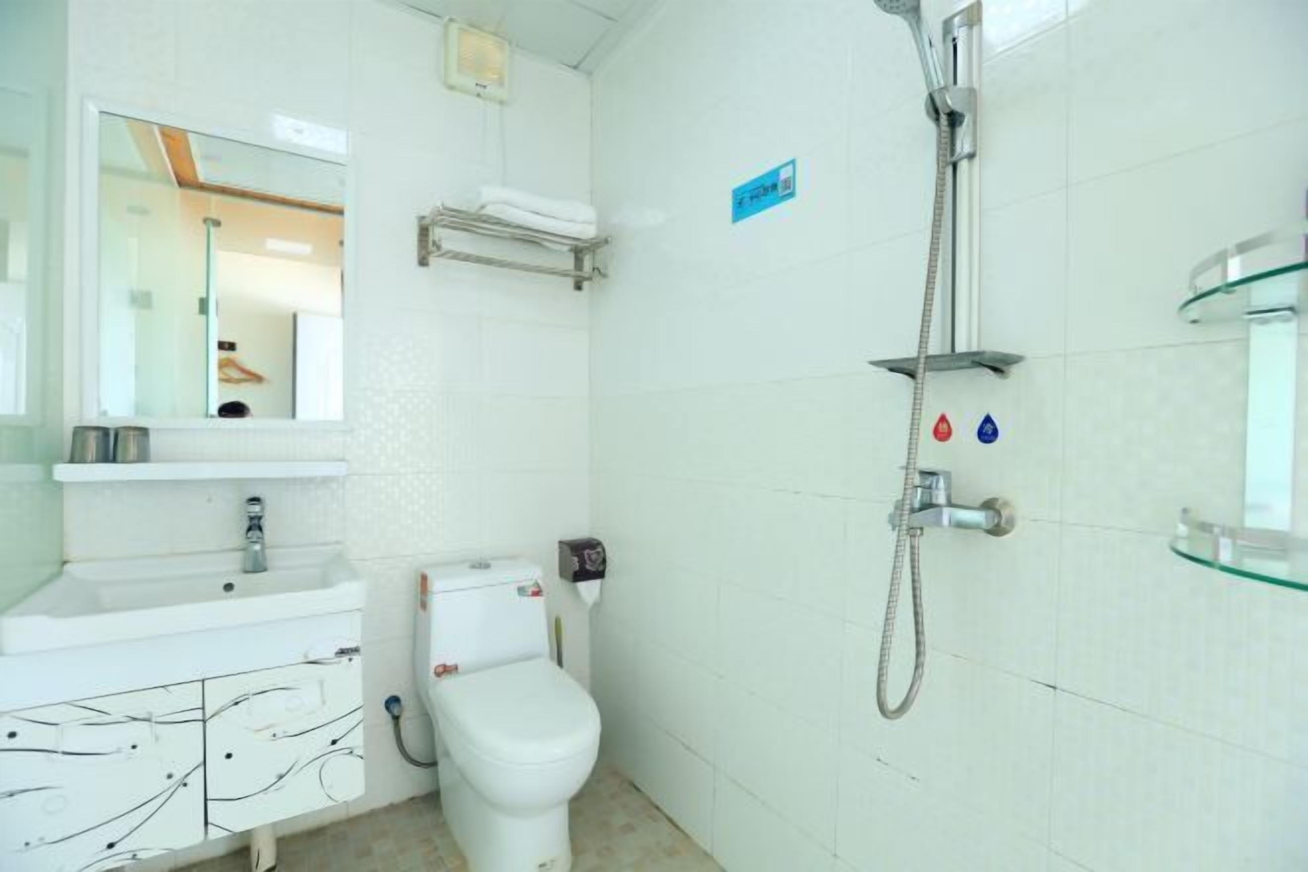 A bathroom with a white sink, toilet, and shower. There is a mirror above the sink and a towel rack on the wall.