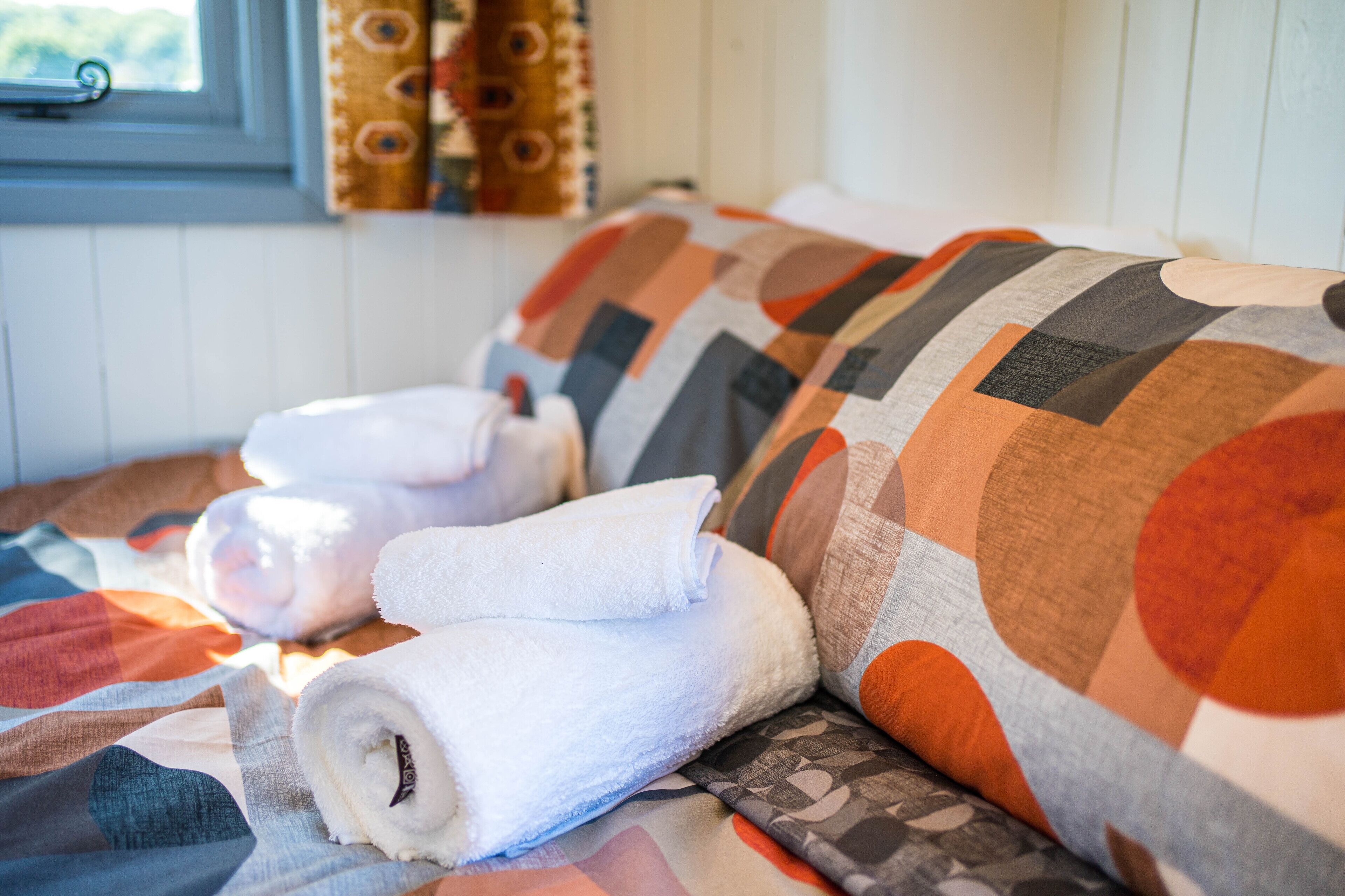 A bed with a patterned blanket and rolled white towels.