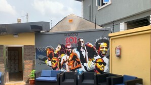 An outdoor seating area with wicker furniture and a mural on the wall. - Treasureland Cottage (Lagos)