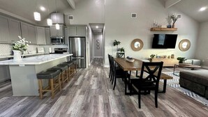 A modern kitchen with a central island, bar stools, and a dining area with a wooden table and chairs. - Blue Haven Beach!! (Freeport)