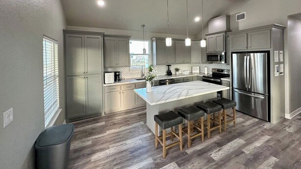 A modern kitchen with grey cabinets, a central island with stools, stainless steel appliances, and a view to the outside. - Blue Haven Beach!! (Freeport)