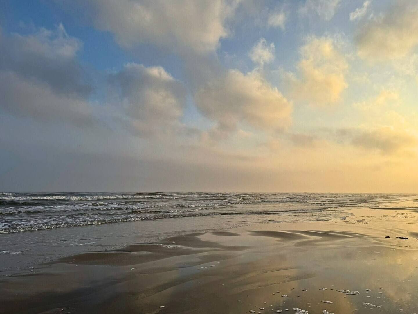Een strand met golven en een bewolkte lucht.