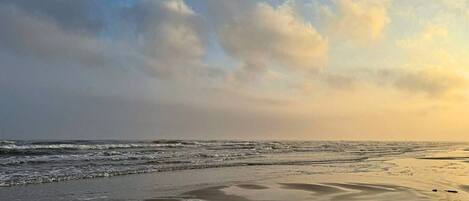Een strand met golven en een bewolkte lucht.