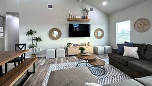 A modern living room with a wooden dining table, a sofa, and a TV mounted on the wall. - Blue Haven Beach!! (Freeport)
