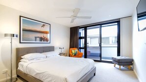 A modern hotel room with a large bed, a ceiling fan, a view of the outside, and a chair with a colorful cushion. - Chic 2-bed Bridgeview Apartments Batemans Bay (Batemans Bay)