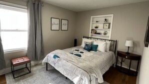 A bedroom with a bed, bedside table, lamp, bench, and a window with curtains. - Peaceful Place in Winston Salem (Winston-Salem)