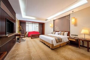 Quarto de hotel com uma cama grande, televisão, secretária e uma cadeira vermelha.