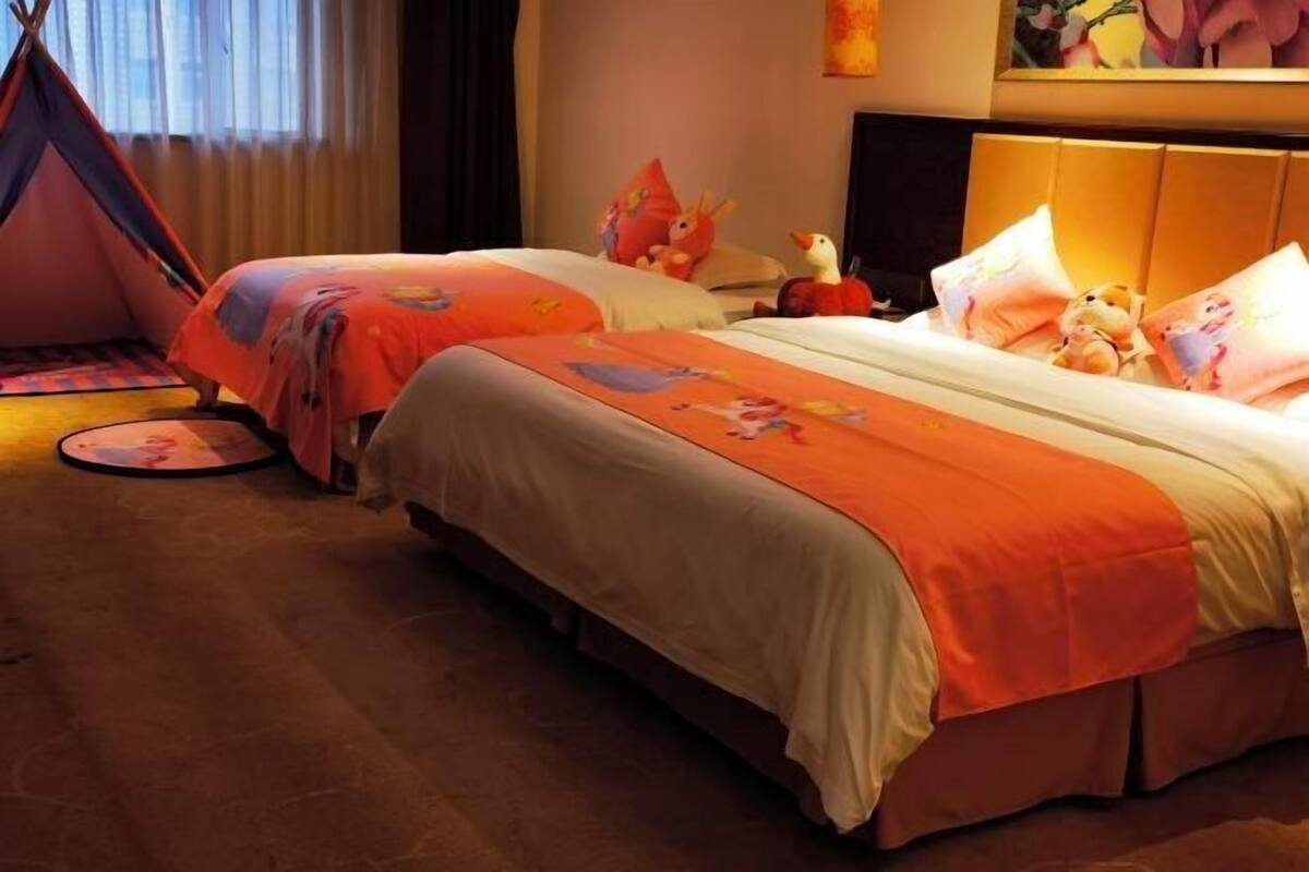 Habitación de hotel con dos camas, cada una con ropa de cama naranja a juego y almohadas con personajes de dibujos animados.