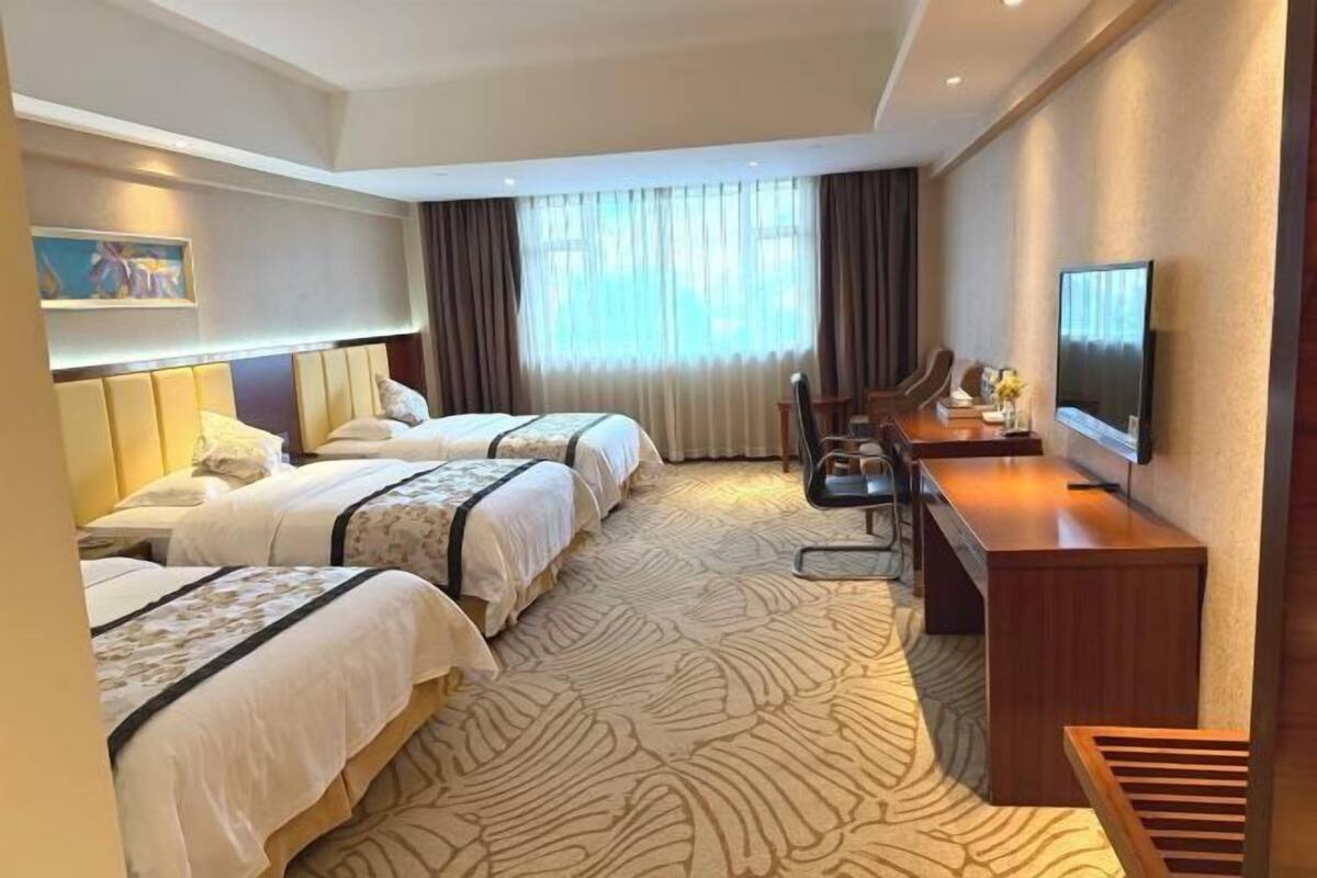 Habitación de hotel con dos camas, un escritorio, una silla, un televisor y un ventanal con cortinas.