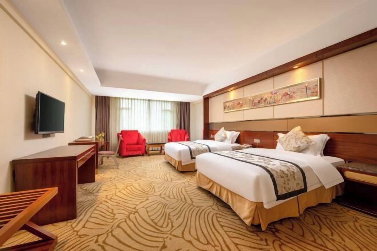 Habitación de hotel con dos camas, televisión, escritorio, una silla roja y un ventanal grande con cortinas.