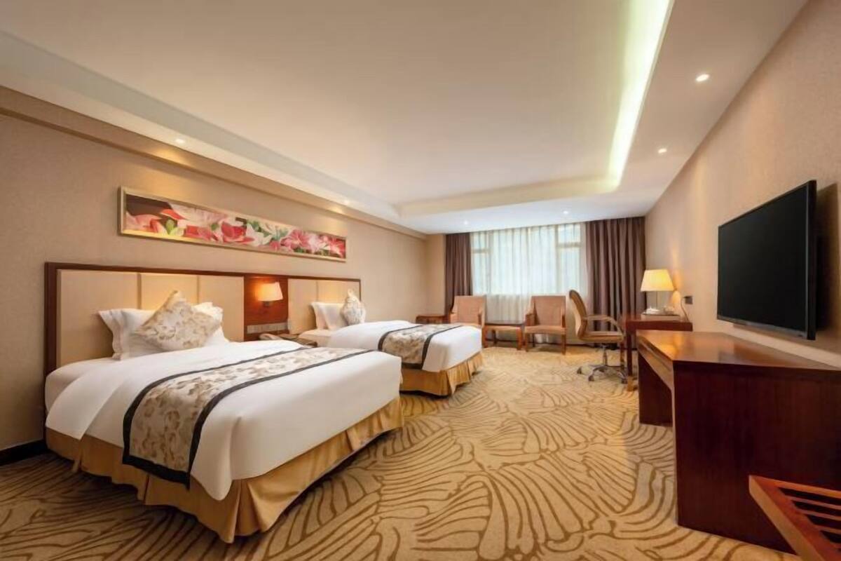 Habitación de hotel con dos camas, un escritorio, una silla, un televisor y un cuadro en la pared.