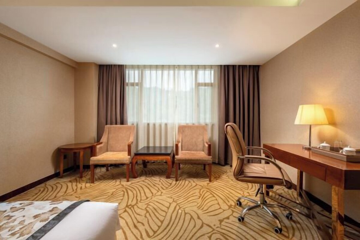 Ein Hotelzimmer mit einem Bett, zwei Sesseln, einem Schreibtisch und einer Lampe.