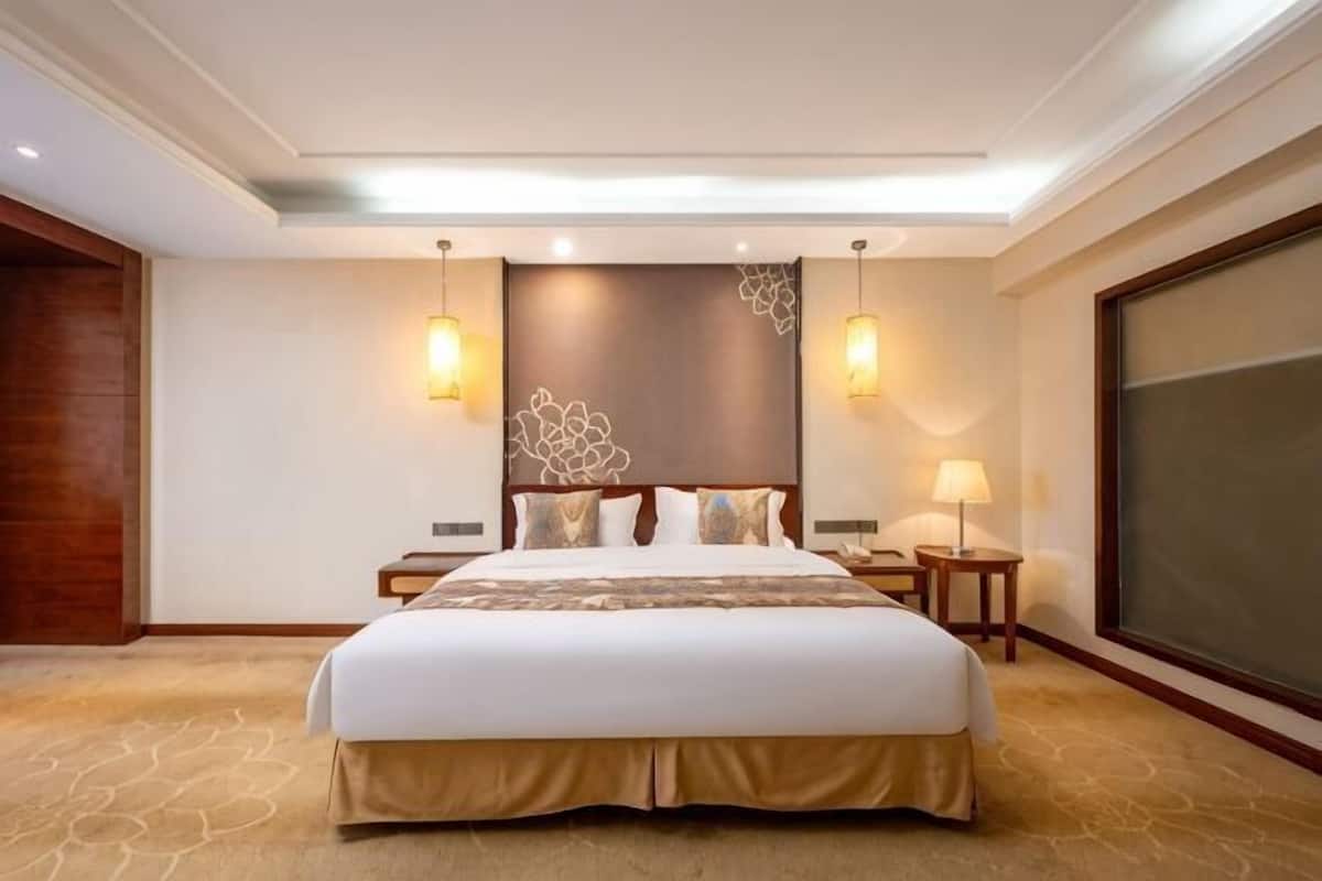 Habitación de hotel con una cama grande, dos mesitas de noche, una lámpara de pared y un ventanal amplio.