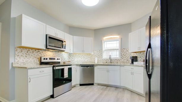 A modern kitchen with white cabinetry, a stainless steel microwave, an oven, and a dishwasher.
