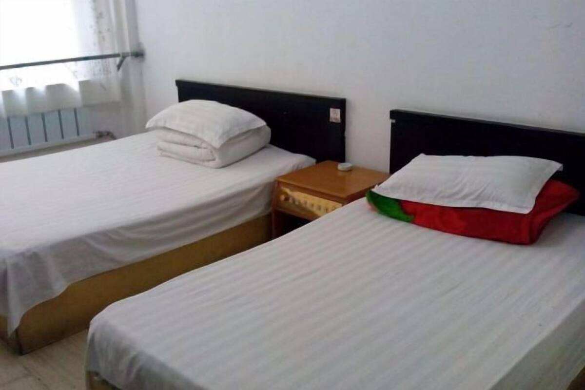 Two single beds with white linens, a wooden nightstand, and a red pillow on one bed.