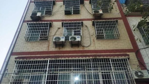 Un edificio de varios pisos con múltiples unidades de aire acondicionado y ventanas con barrotes.