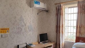 Una habitación con escritorio, computadora, cama, ventana con cortinas, aire acondicionado y un cartel que indica disponibilidad de Wi-Fi.