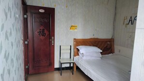 Una habitación con puerta de madera, una cama con ropa blanca, una pequeña silla blanca y una pared con un cartel.