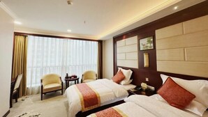 Una habitación de hotel con dos camas, un ventanal con cortinas, una mesita y una silla.