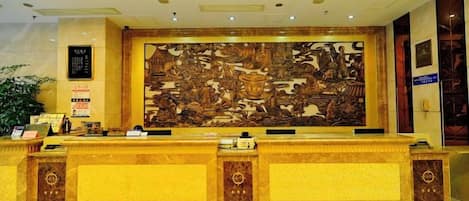 A reception desk with a large mural, a digital display, and a potted plant.