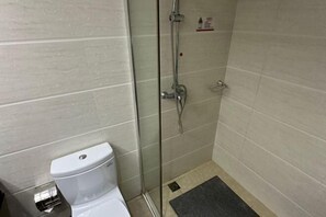 Ein Badezimmer mit Toilette, einer Duschkabine aus Glas und einem kleinen Ablagebereich für Kosmetikartikel.