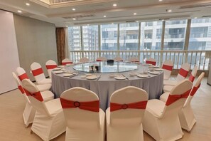 A conference room with a round table, white chairs with red sashes, and a city view through large windows. - Overseas Chinese Hotel (Anxi)