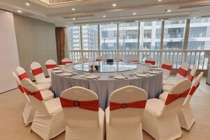 A conference room with a round table, white chairs with red sashes, and a city view through large windows.
