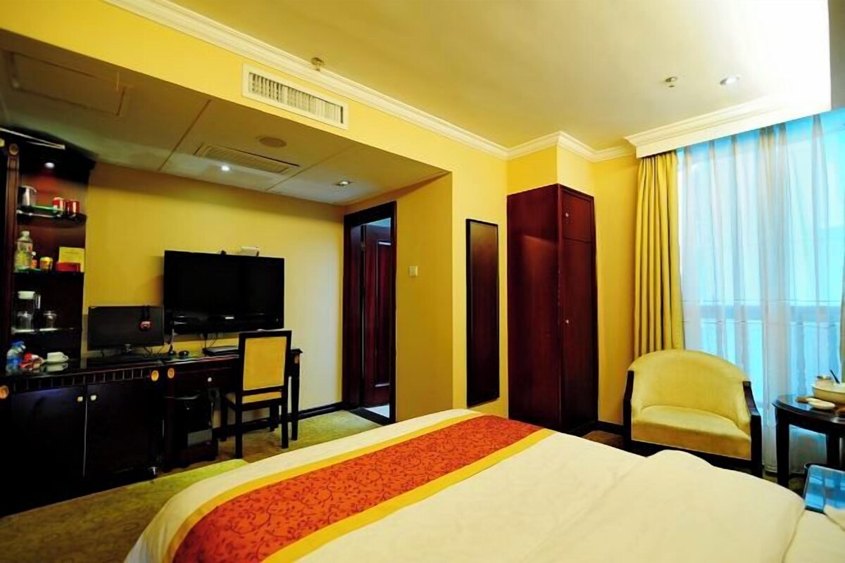 A hotel room with a bed, a desk, a chair, a television, and a wardrobe.