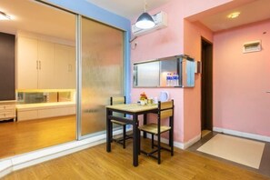 Een kamer met een schuifdeur naar een keuken, een klein tafeltje met stoelen, een hangende airconditioner en een raam met uitzicht.