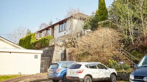 A residential area with parked cars, a house with a balcony, and a steep hill. - Fort William Central Self Catering House# (Fort William)