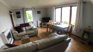 A living room with a sofa, a TV, and a dining area with chairs and a table. - Fort William Central Self Catering House# (Fort William)
