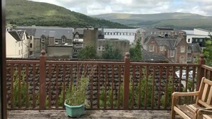 A balcony with a wooden railing, a potted plant, and a wooden bench. - Fort William Central Self Catering House# (Fort William)