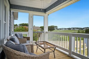 A covered porch with wicker furniture and a glass table, overlooking a residential area with houses and greenery.