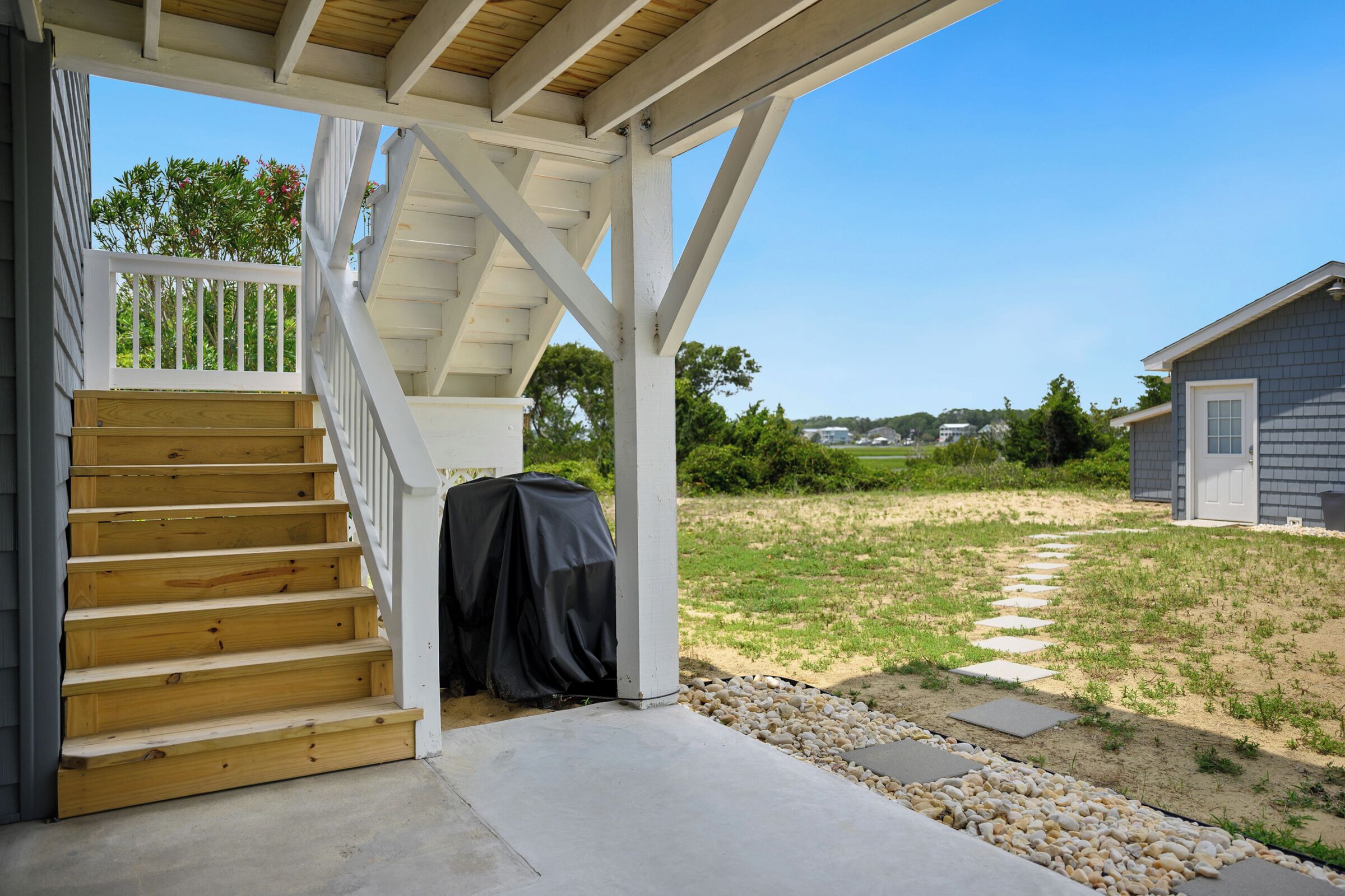 A covered outdoor staircase leading to a wooden deck, with a covered grill and a house in the background.