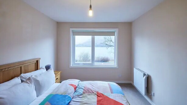 A bedroom with a bed, a window, and a radiator. - Etive, Beautiful Lochside Apartment with balcony (Fort William)