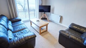 A living room with a sofa set, a coffee table, and a television on a stand. - Etive, Beautiful Lochside Apartment with balcony (Fort William)