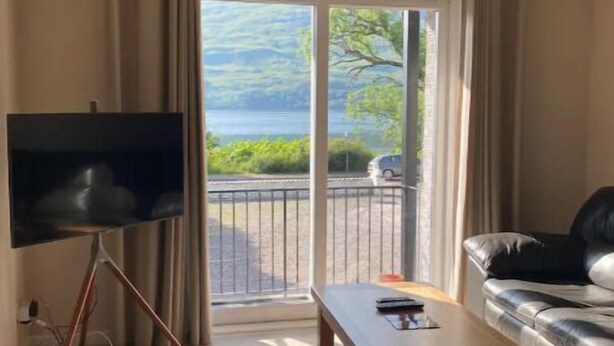 Una sala de estar con televisor, sofá, mesa de centro y vista a un cuerpo de agua a través de una puerta corrediza.
