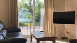 Una sala de estar con un sofá de cuero negro, una mesa de centro de madera y un televisor de pantalla plana sobre un soporte tipo trípode.
