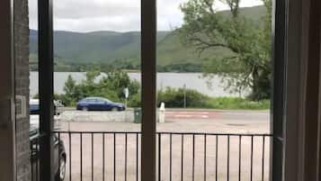 Blick aus einem Fenster mit Metallgitter auf einen Parkplatz und ein Gewässer, im Hintergrund Hügel.