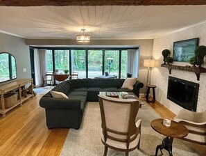 Relax in the living room with a large sectional sofa, armchair, and fireplace, offering a view of the surrounding greenery.